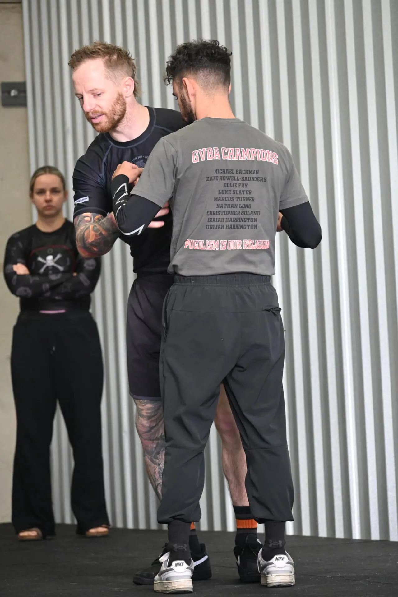 Coach demonstrating a grappling technique with a member while another watches