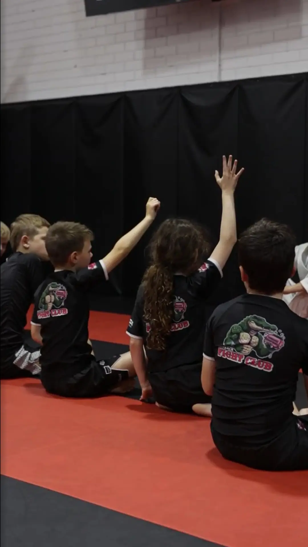 Kids sitting on the mats with hands raised in class