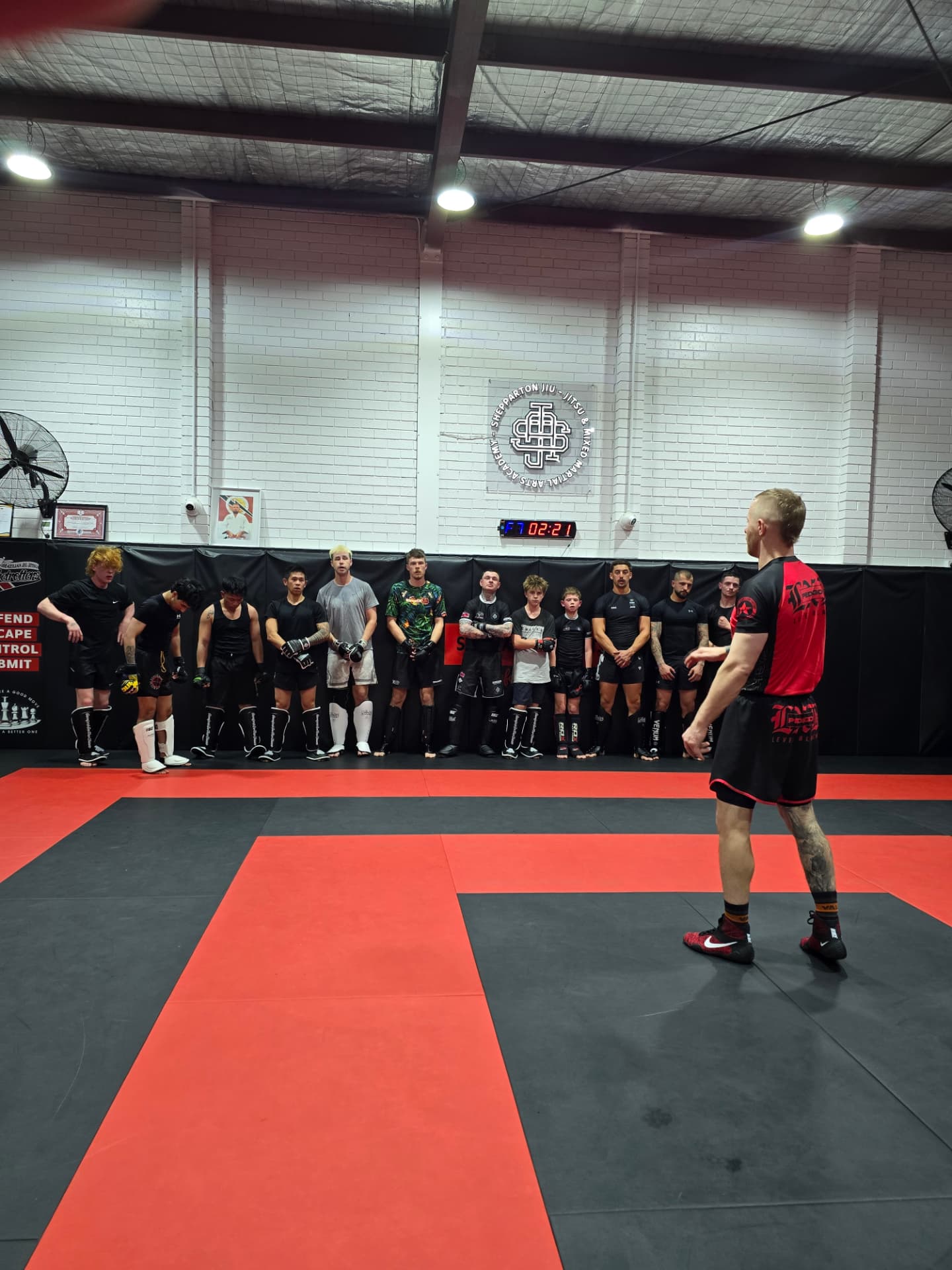 Members lined up along the wall of the Shepparton Jiu-Jitsu mat room as the coach talks to the group